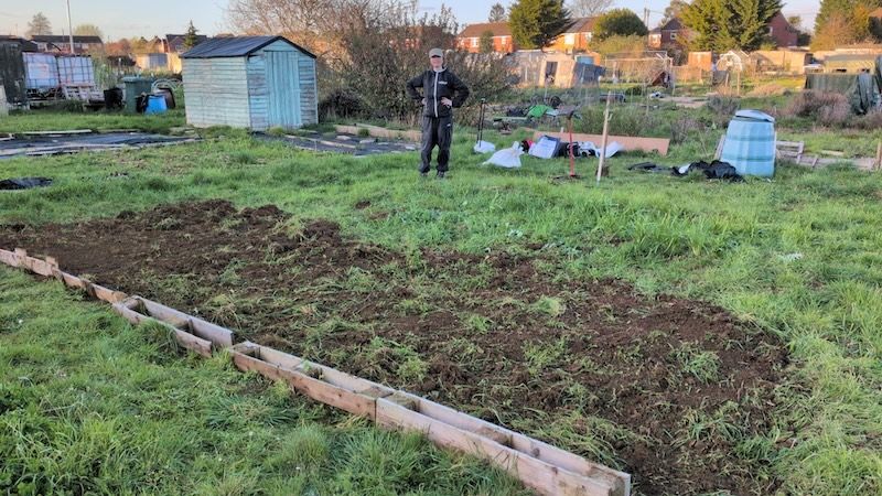 Grace standing with the allotment plot in front of her and one strip dug out.
